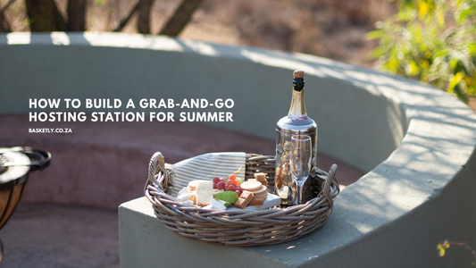 Rattan tray with handles holding a cheese platter, sparkling wine and a glass on an outdoor patio wall
