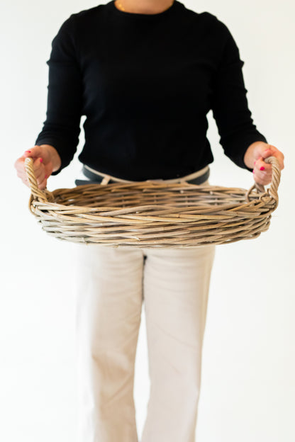 Person holding a rattan tray against a plain background