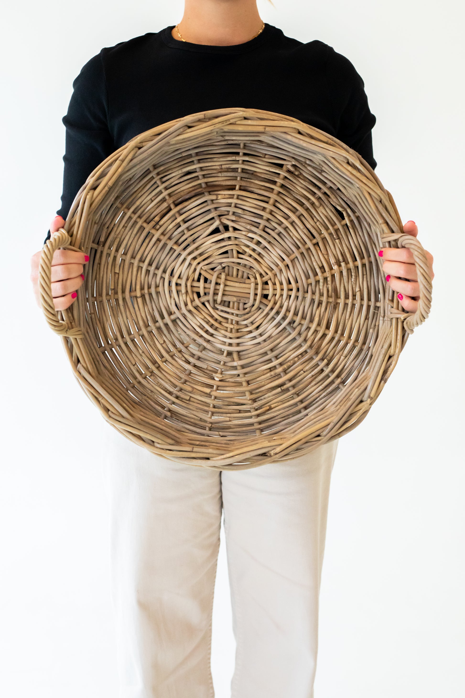 A round, handwoven rattan tray with handles, in a natural grey color, displayed on a white background.