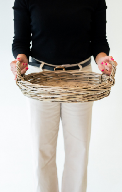 Person holding a rattan tray against a plain background