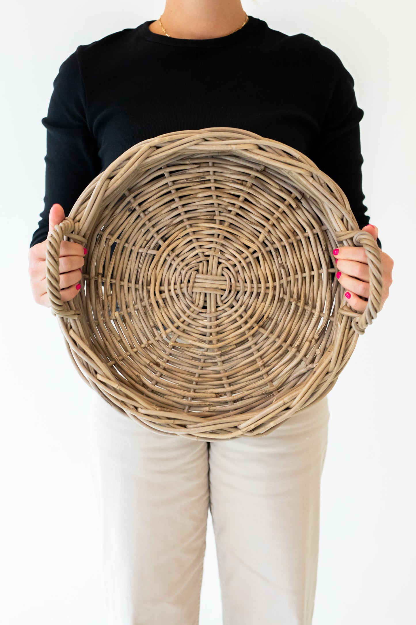 A round, handwoven rattan tray with handles, in a natural grey color, displayed on a white background.