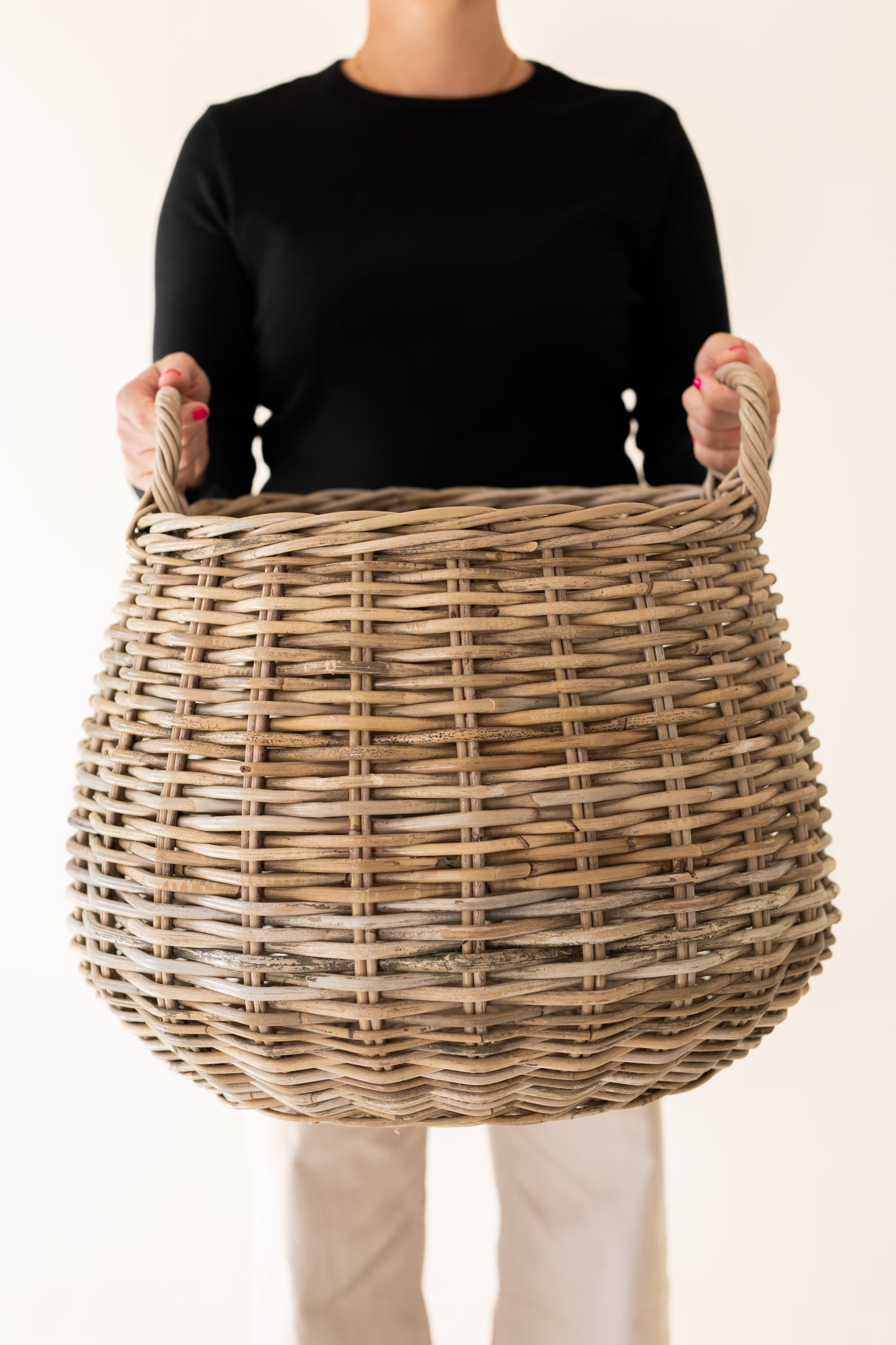 Person holding a wicker basket against a plain background