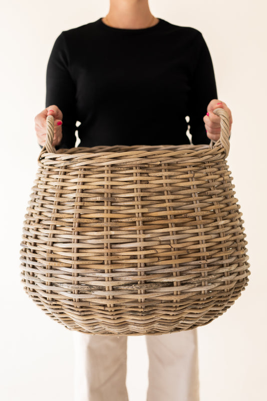 Person holding a wicker basket against a plain background