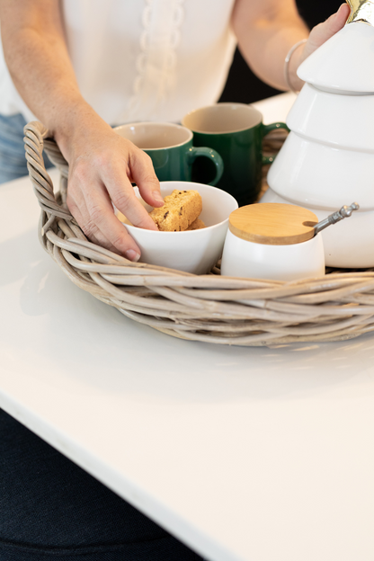 Person holding a cookie over a bowl with tea and cookies on a table in Ratan Tray.