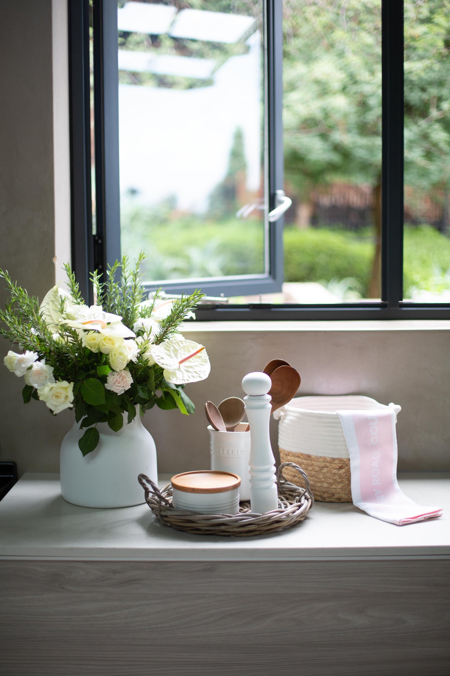 Decorative items in Rattan tray on a windowsill with a view of greenery outside