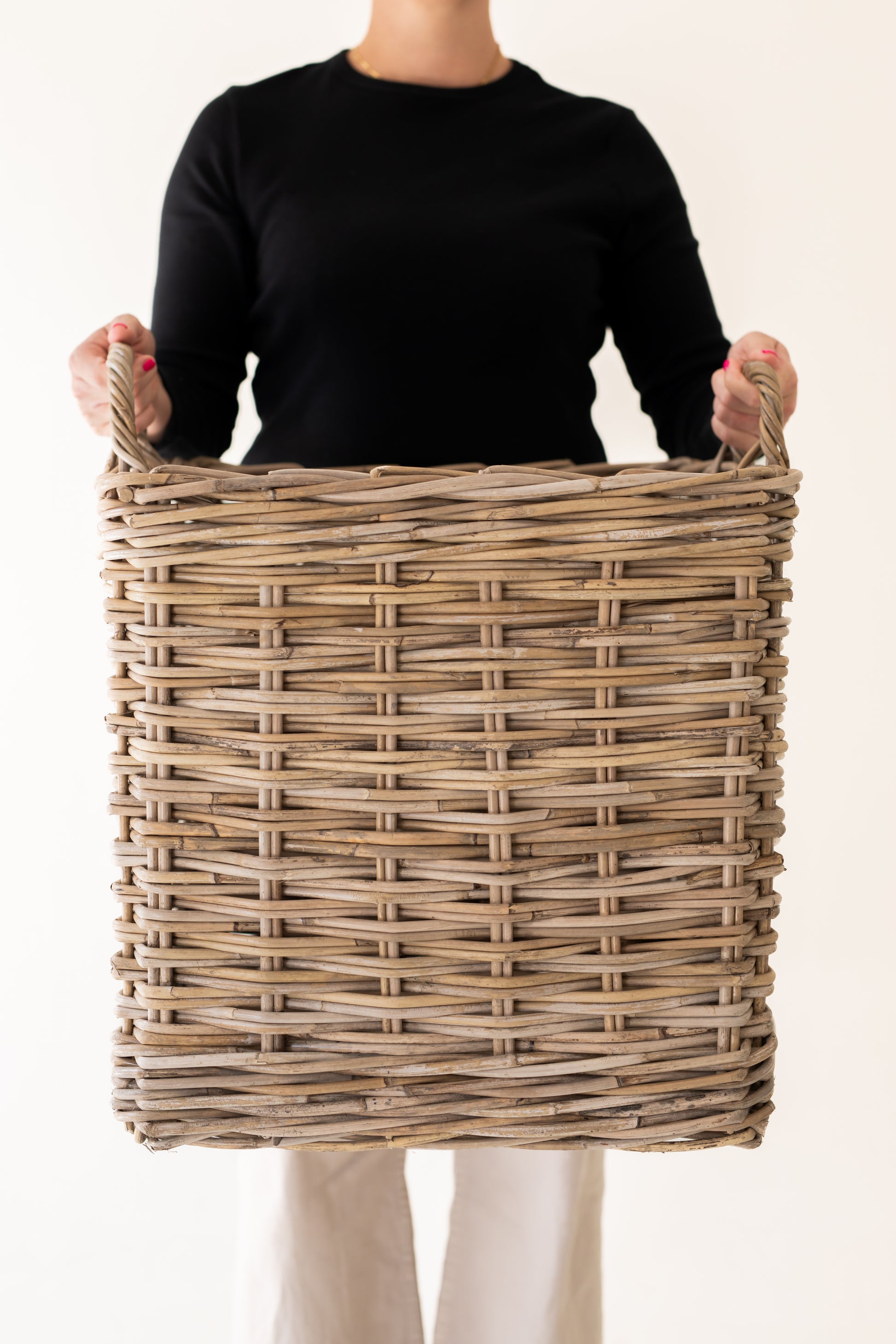 Person holding a large rattan basket against a plain background