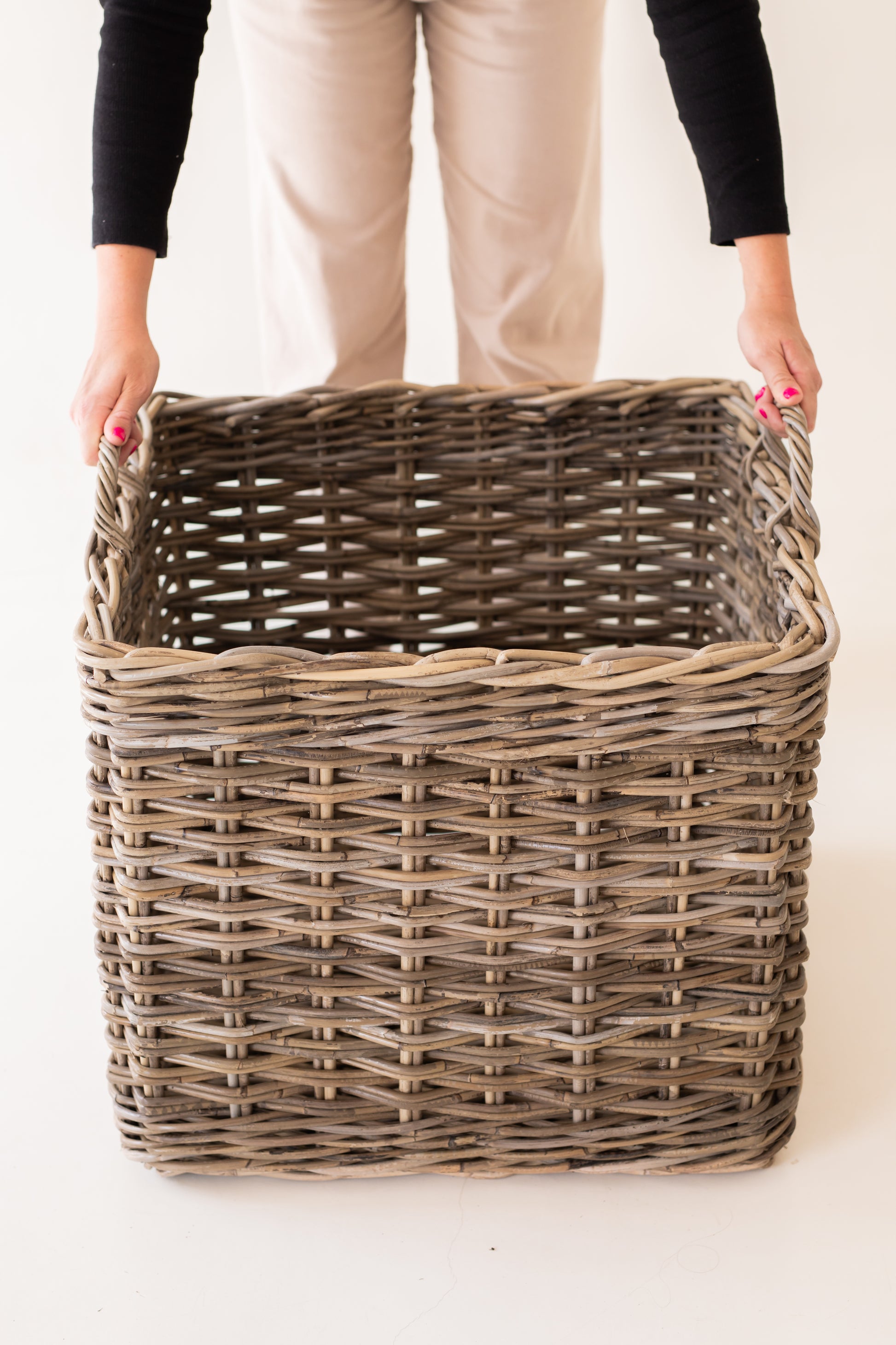 Person holding an extra-large  rattan basket against a plain background