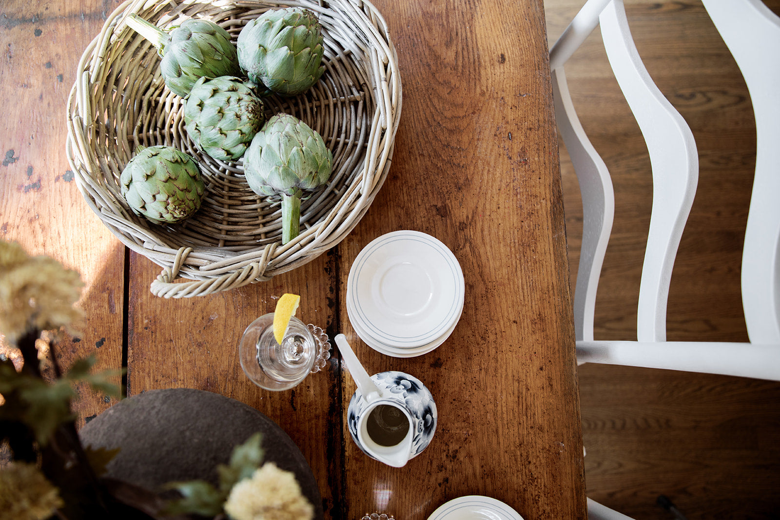 Rattan Tray with green artichokes on a wooden table with a glass of water and lemon.