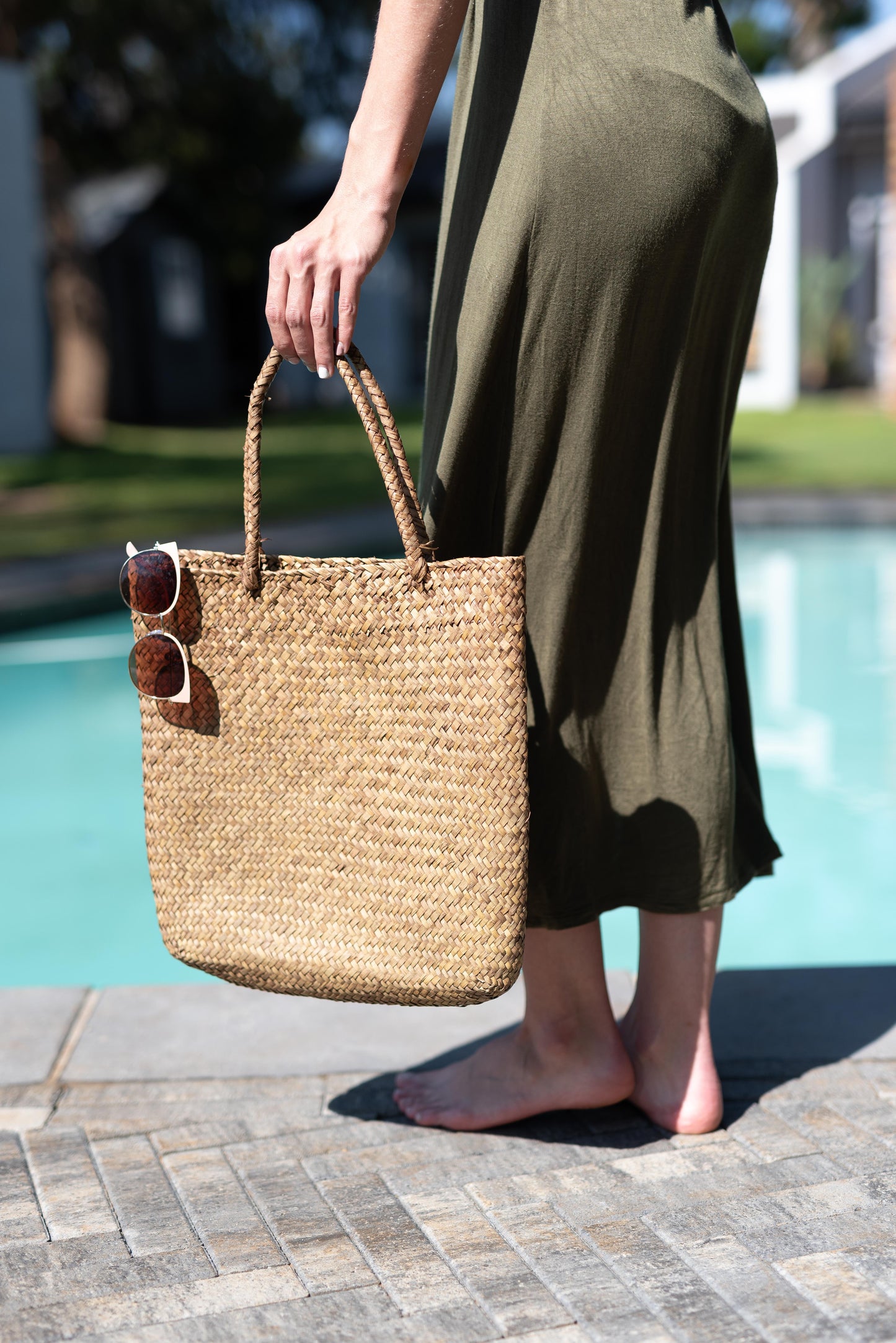 Person holding a woven bag by a poolside