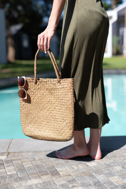 Person holding a woven bag by a poolside