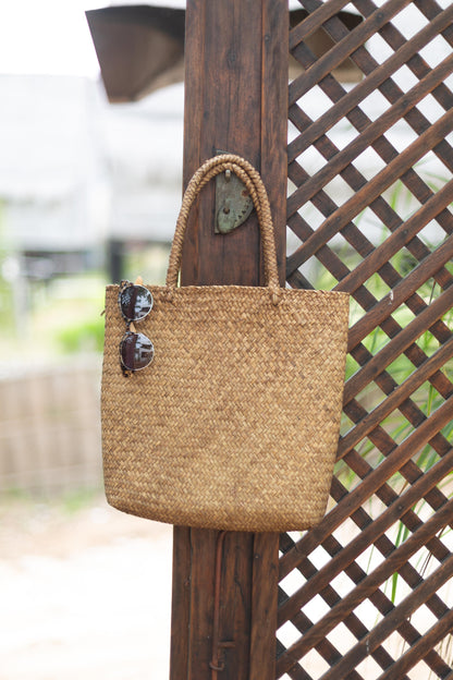 Woven handbag with sunglasses on a wooden post against a lattice background