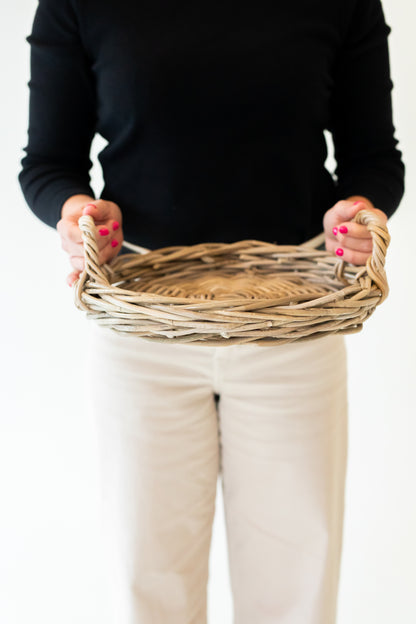 Person holding a rattan tray against a plain background