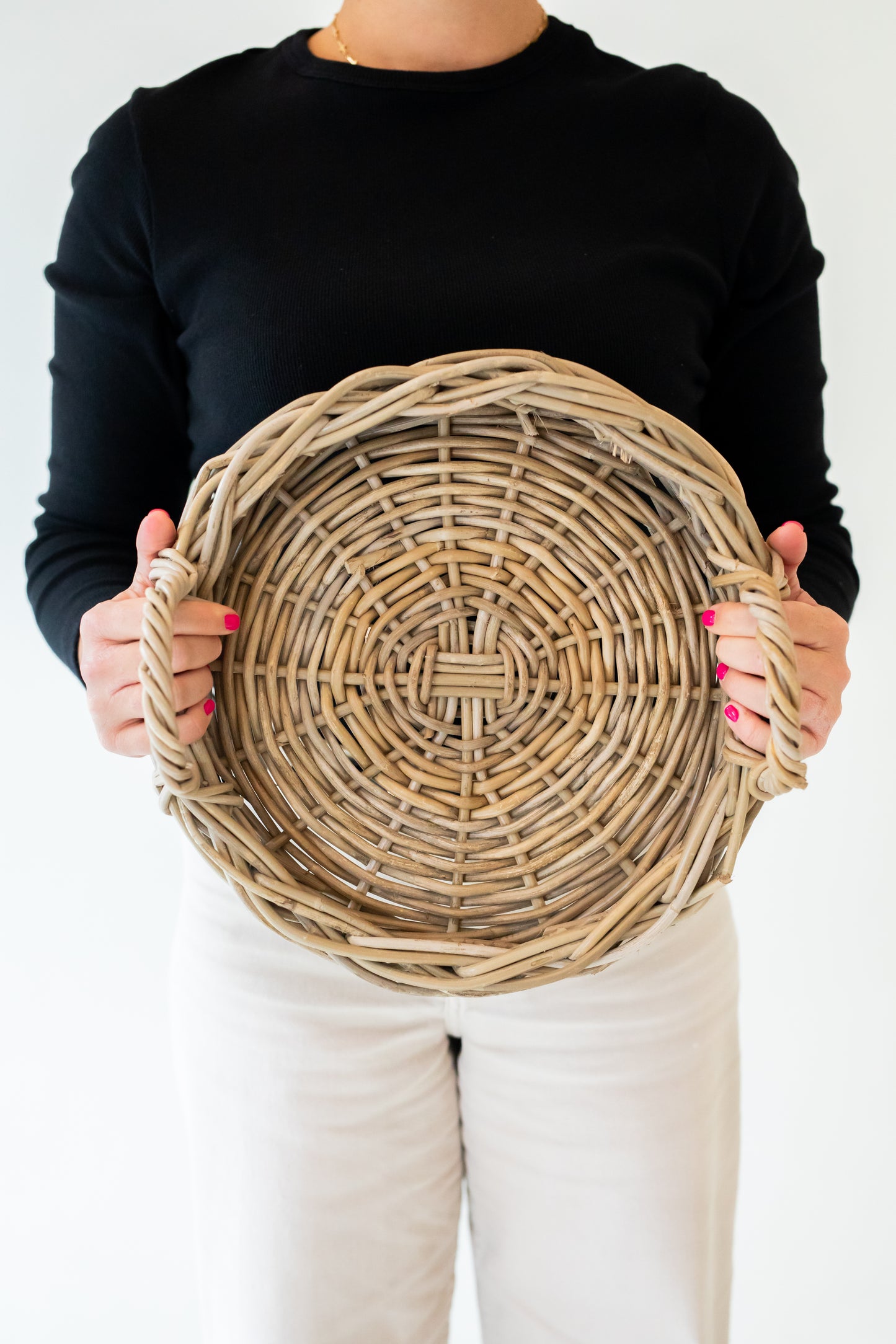 A round, handwoven rattan tray with handles, in a natural grey color, displayed on a white background.