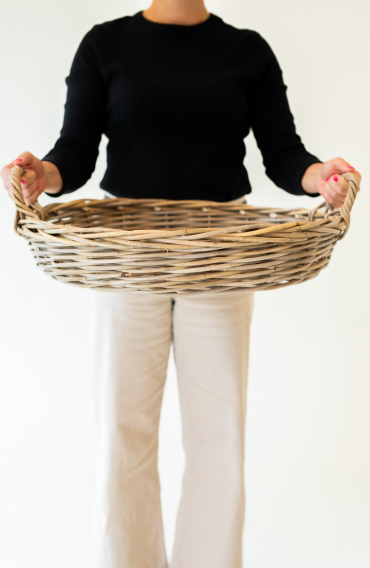 Person holding a rattan tray against a plain background