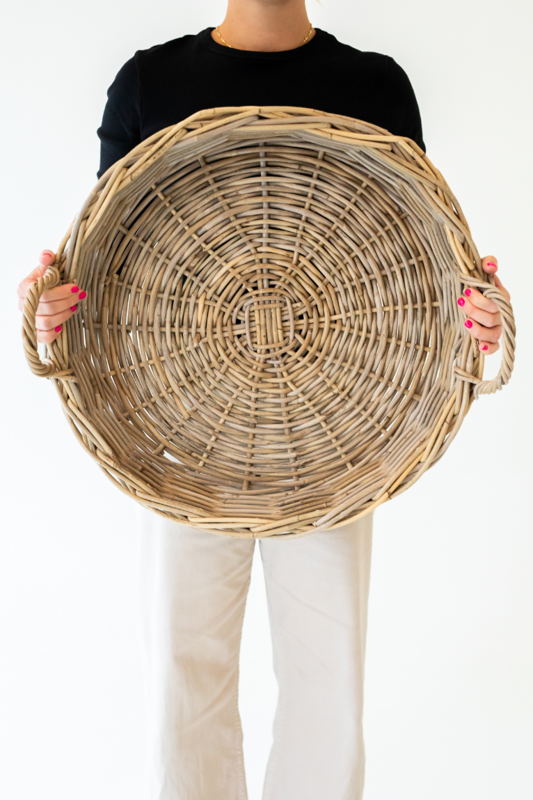 Person holding a large rattan tray against a plain background
