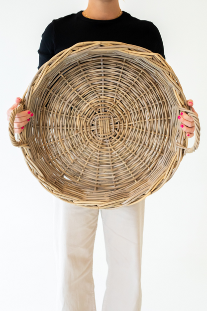 Person holding a large rattan tray against a plain background